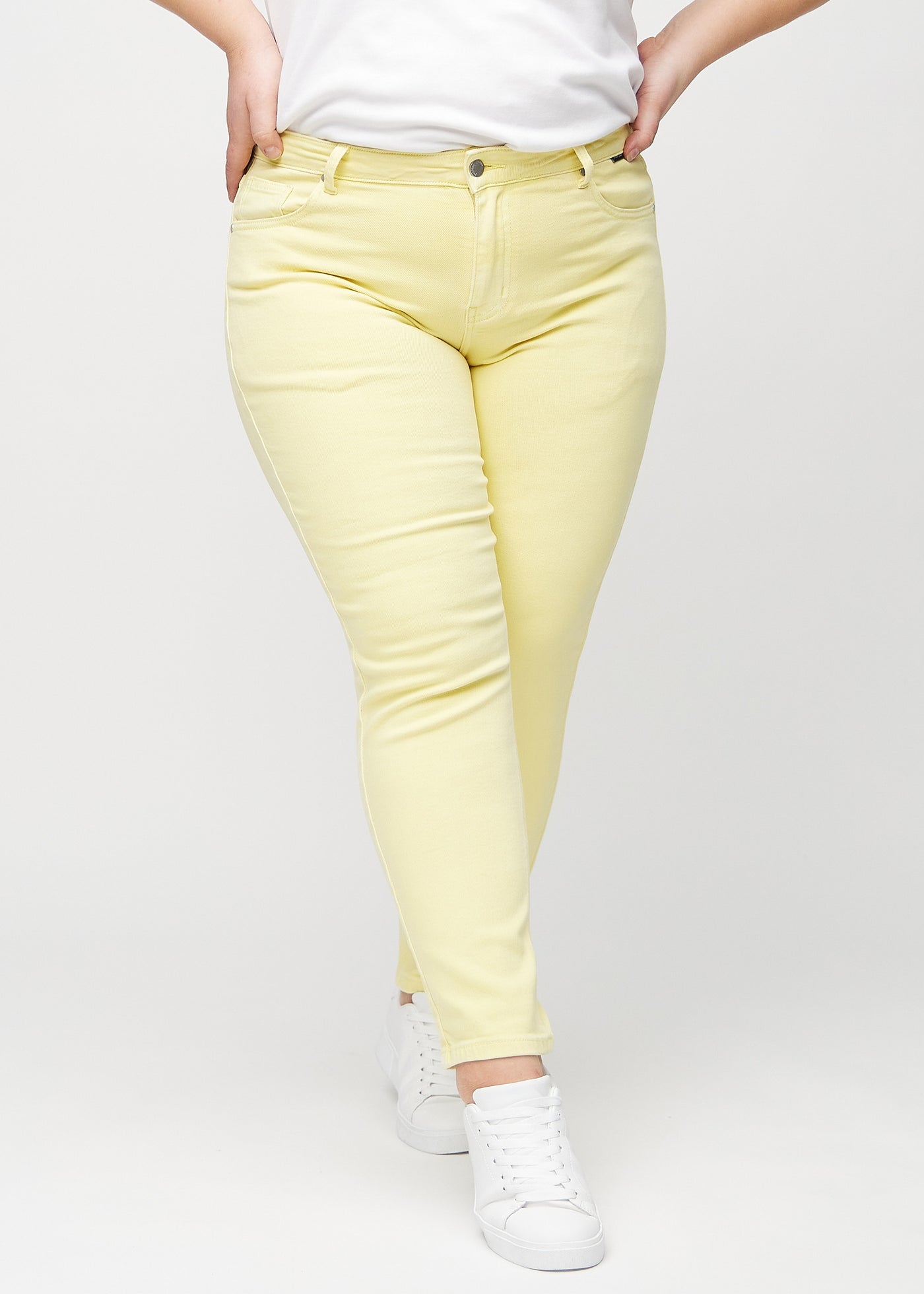 Lysegule slim jeans, modelnavn Lemonades, som sidder tæt til benet, dog lidt løsere ved anklen, på en plus-size model, set forfra.